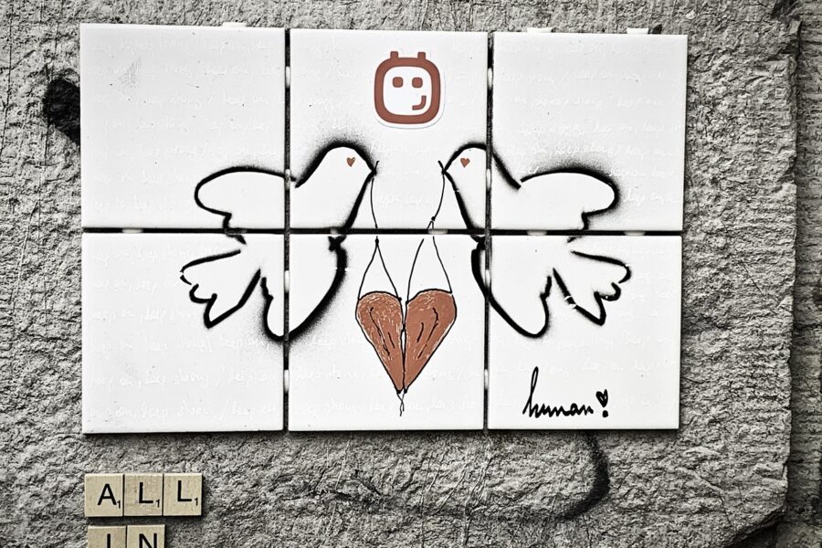 two doves facing each other drawn across 6 white tiles, holding a red heart between them. "All in" in the left corner, in wooden tiles.